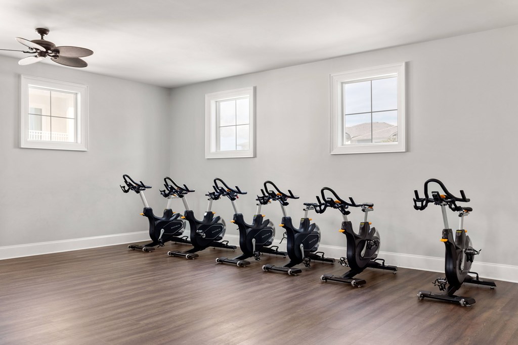 A room with a row of stationary bikes and a ceiling fan.