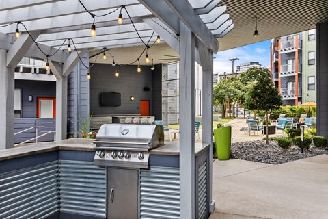 A BBQ grill is on a patio with a green trash can and a tree.