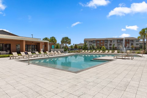A large pool surrounded by a tiled patio and lounge chairs.