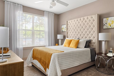 A bedroom with a large bed, a ceiling fan, and a window with white curtains.