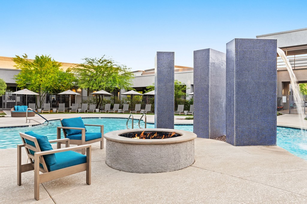 A poolside area with a fire pit, chairs, and umbrellas.
