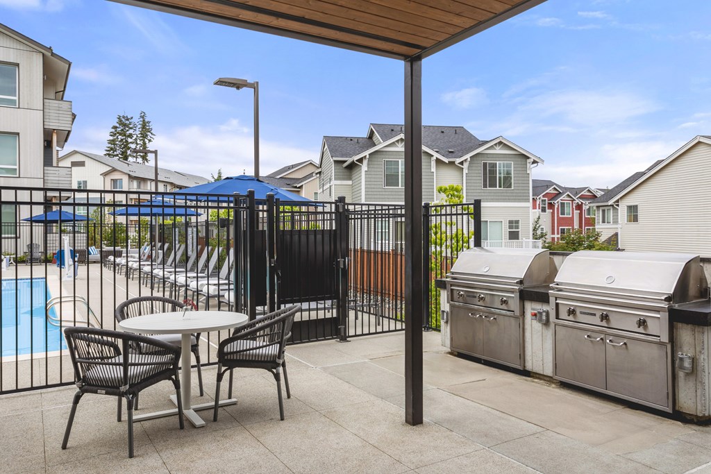 A patio with a table and chairs is surrounded by a pool and houses.