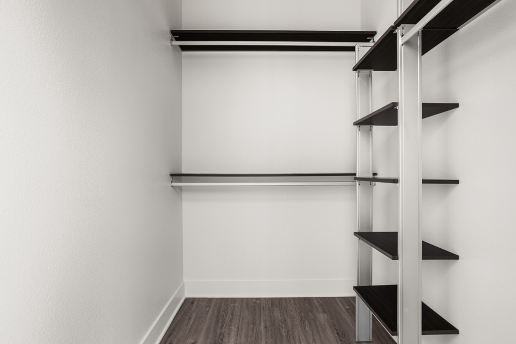A white wall with a shelf and a wooden floor.