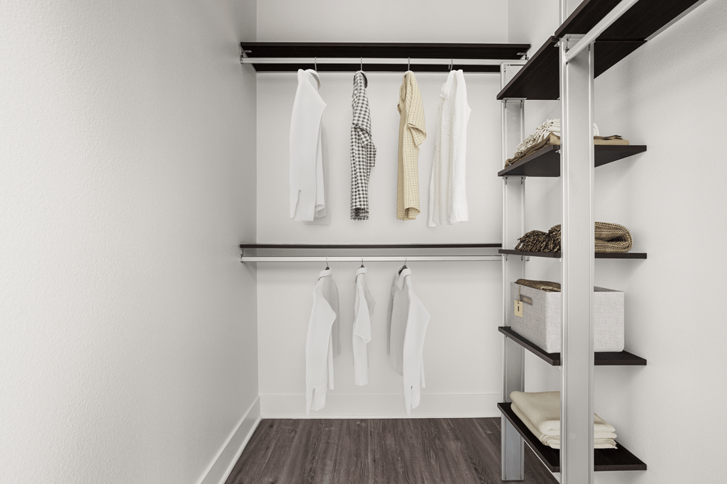 A white closet with clothes hanging and shelves with baskets and towels.