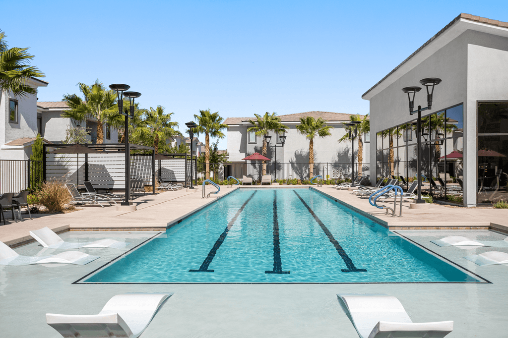 A swimming pool with a clear blue water and white lounge chairs.