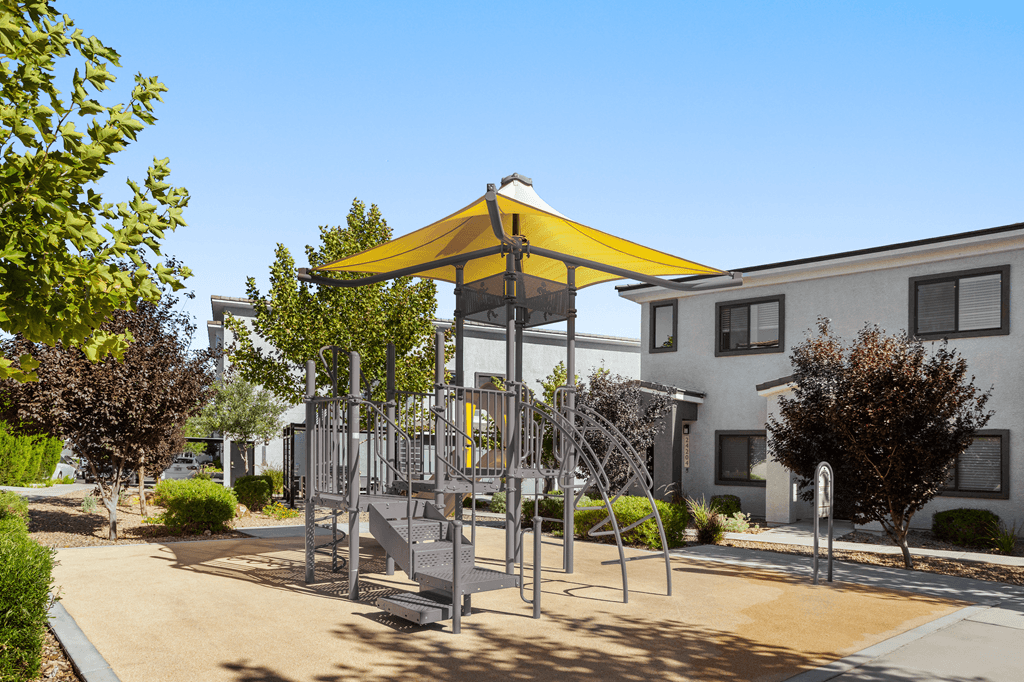 A playground with a yellow canopy is situated in front of a building.