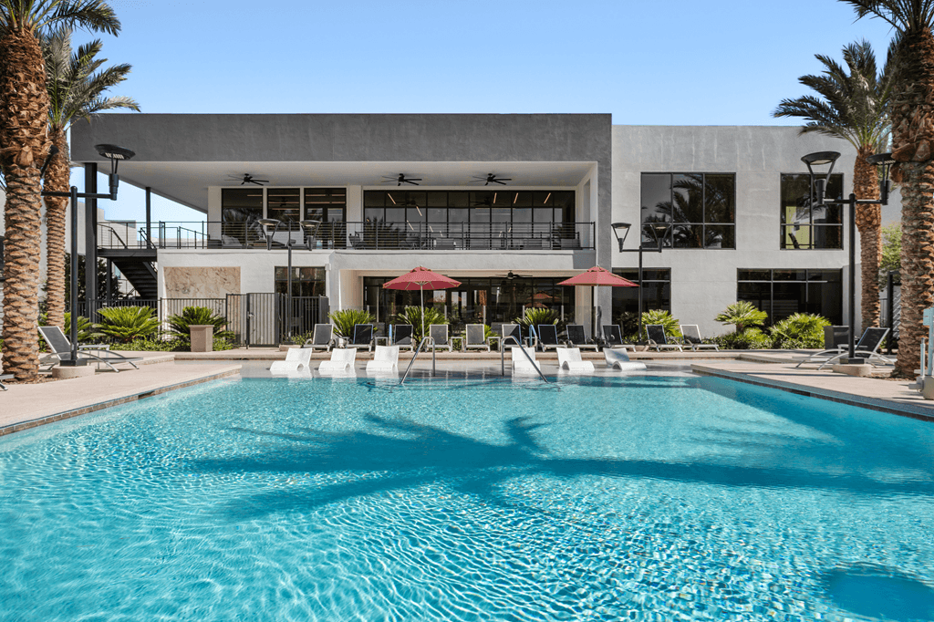 A large swimming pool in front of a modern building with palm trees around it.