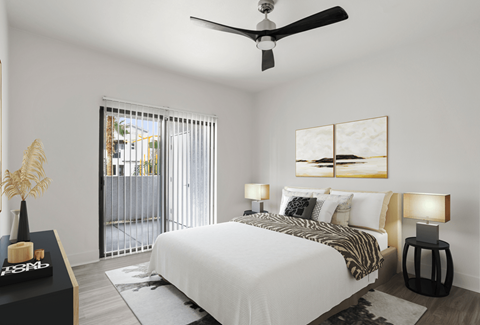 A bedroom with a large bed, a ceiling fan, and a view of the outdoors through a sliding glass door.