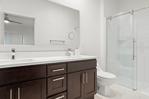 A white toilet sits in a bathroom with a white sink and brown cabinets.
