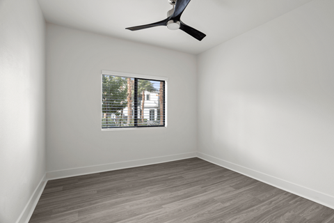 A room with a ceiling fan and a window showing a view of trees and a building outside.