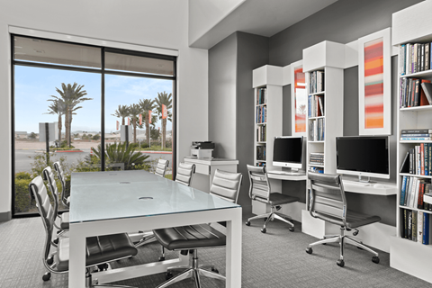 A modern office with a glass table and chairs, a bookshelf, and a view of the outdoors.