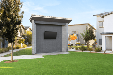 A modern house with a grey facade and a small window is surrounded by a well-kept lawn and other houses.