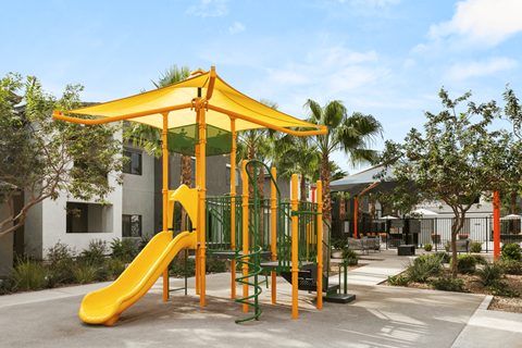 A playground with a yellow slide and a green canopy.