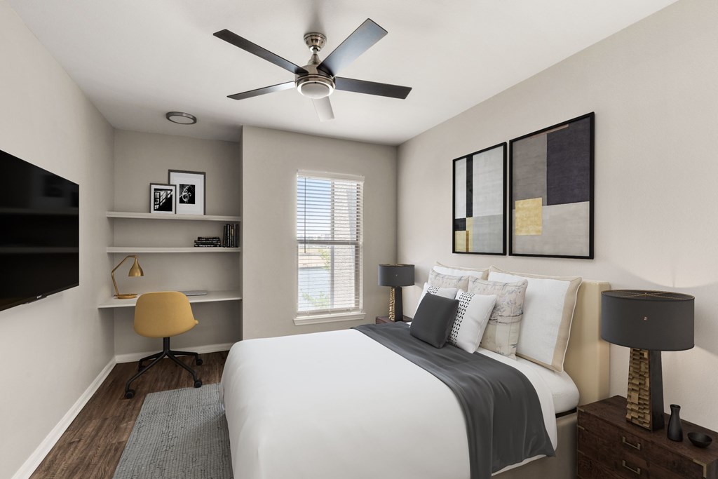 A bedroom with a bed, a desk with a chair, and a ceiling fan.