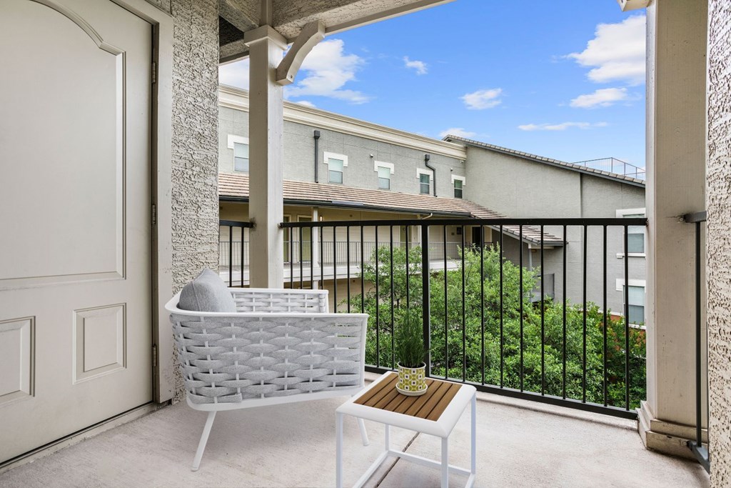 A white chair and table are on a balcony with a view of a building.