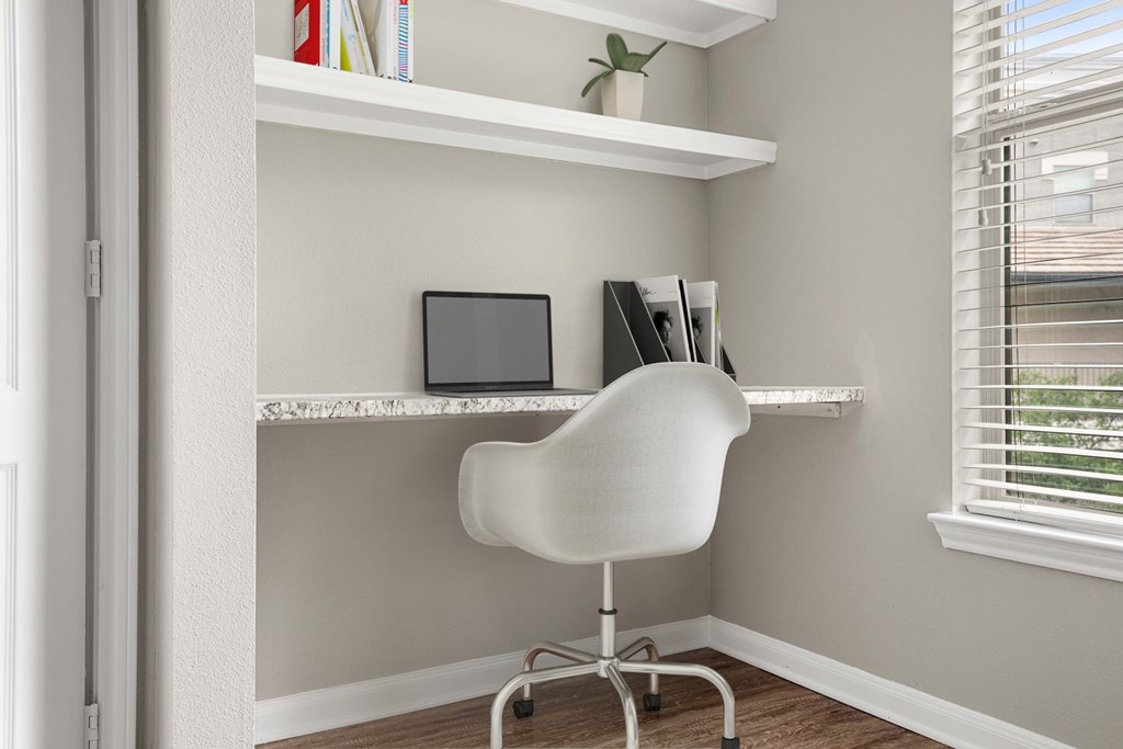 A white chair is in front of a desk with a laptop and a plant on it.