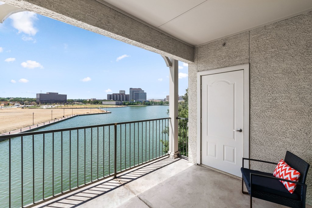 A balcony with a white door and a black chair with a red and white pillow.