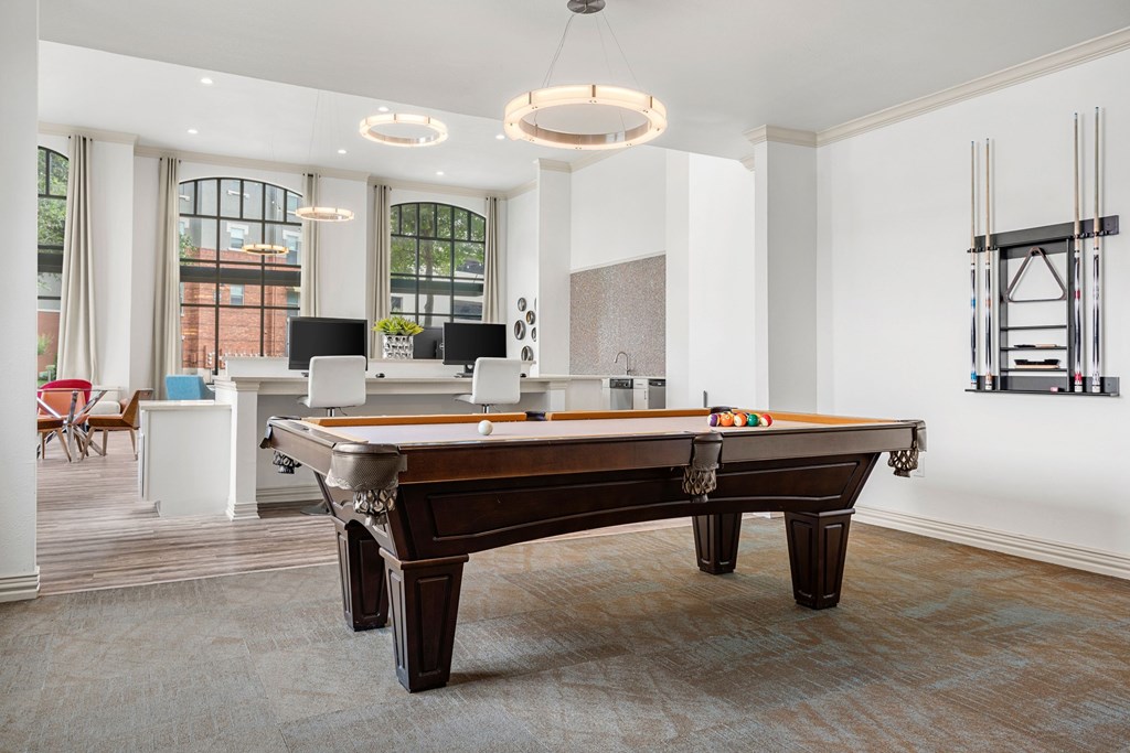 A pool table is in the middle of a room with a white ceiling and a window.
