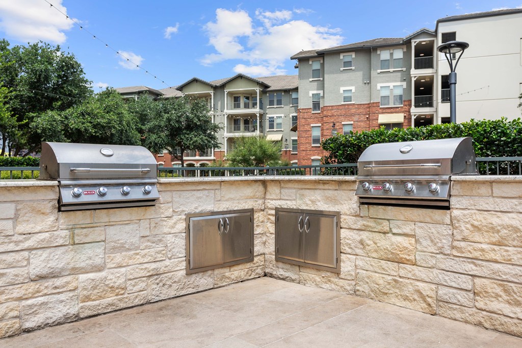 Two outdoor grills are built into a stone wall.