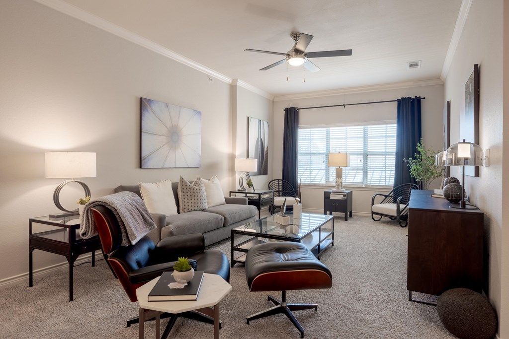 A living room with a grey sofa, a black leather chair, a white coffee table, and a ceiling fan.