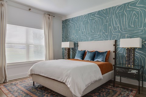 A bedroom with a white bed and a patterned wallpaper.