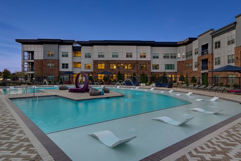 A large swimming pool with lounge chairs and a colorful sculpture in front of a multi-story apartment building.