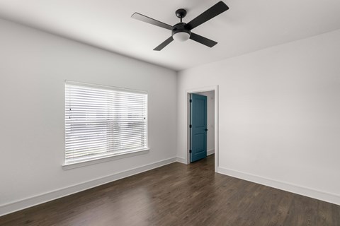 A room with a ceiling fan, a window with blinds, and a blue door.