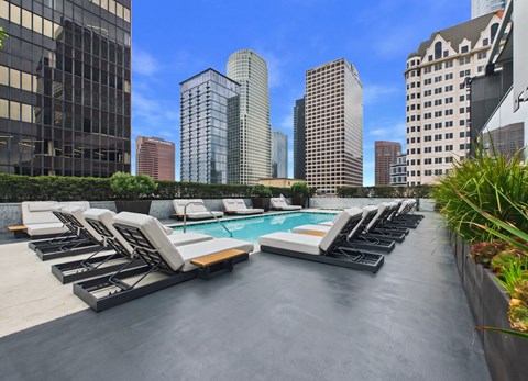 A rooftop pool area with lounge chairs and a city skyline in the background.
