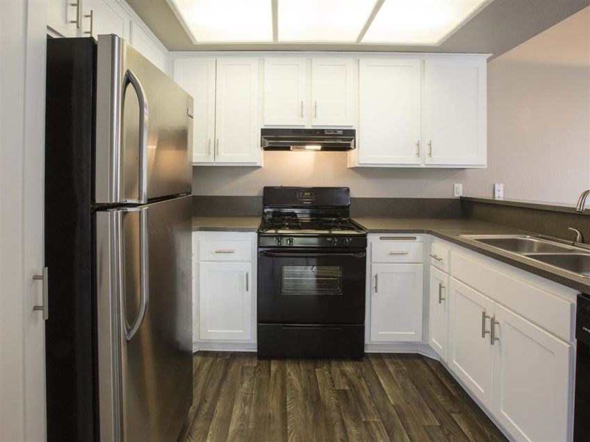 A black refrigerator is in a kitchen with white cabinets.