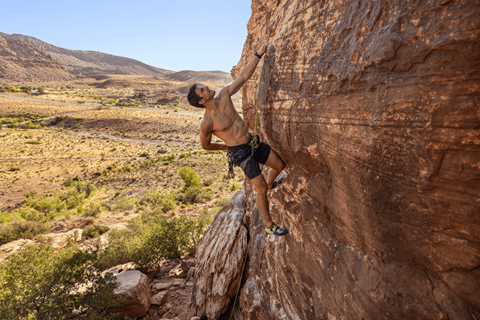 A man climbing a rock face in a desert landscape.