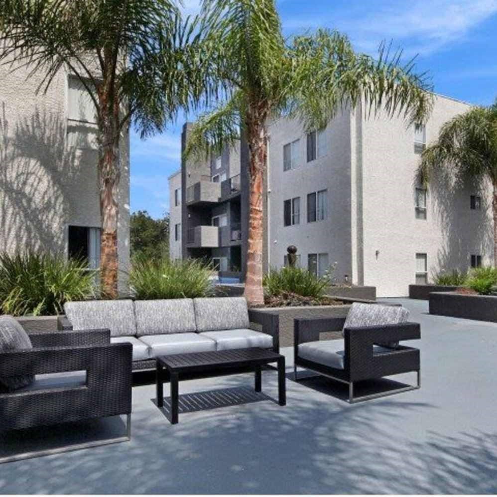 A patio with furniture and palm trees in front of a building.
