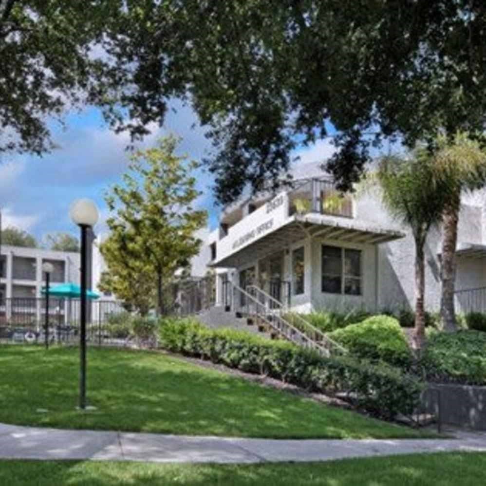 A white building with a green awning is surrounded by trees and bushes.