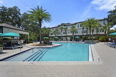 A large swimming pool surrounded by a brick patio and palm trees.