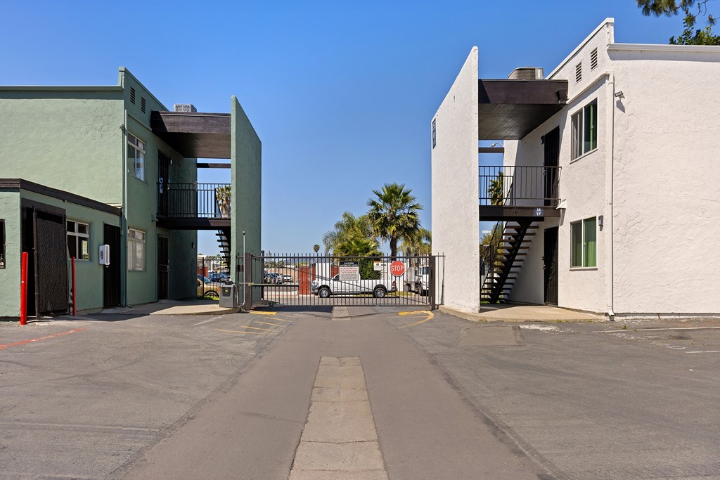 A parking lot with a green building on the left and a white building on the right.