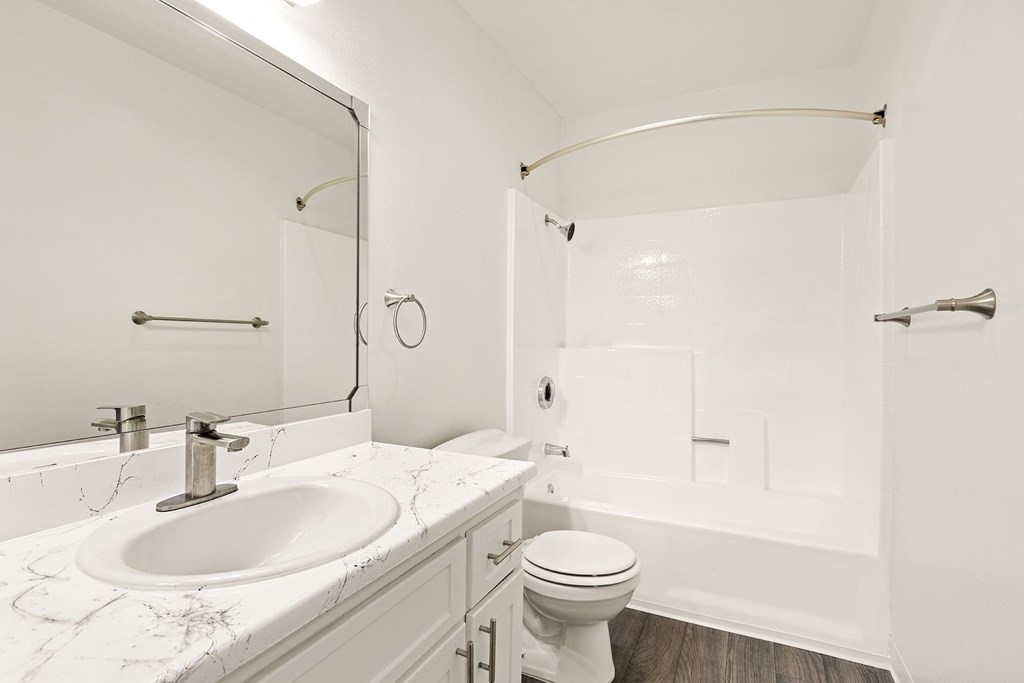 A white bathroom with a marble counter top and a white toilet.