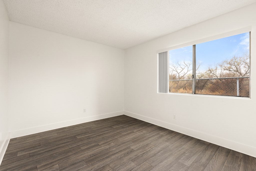Empty room with a large window and wooden flooring.