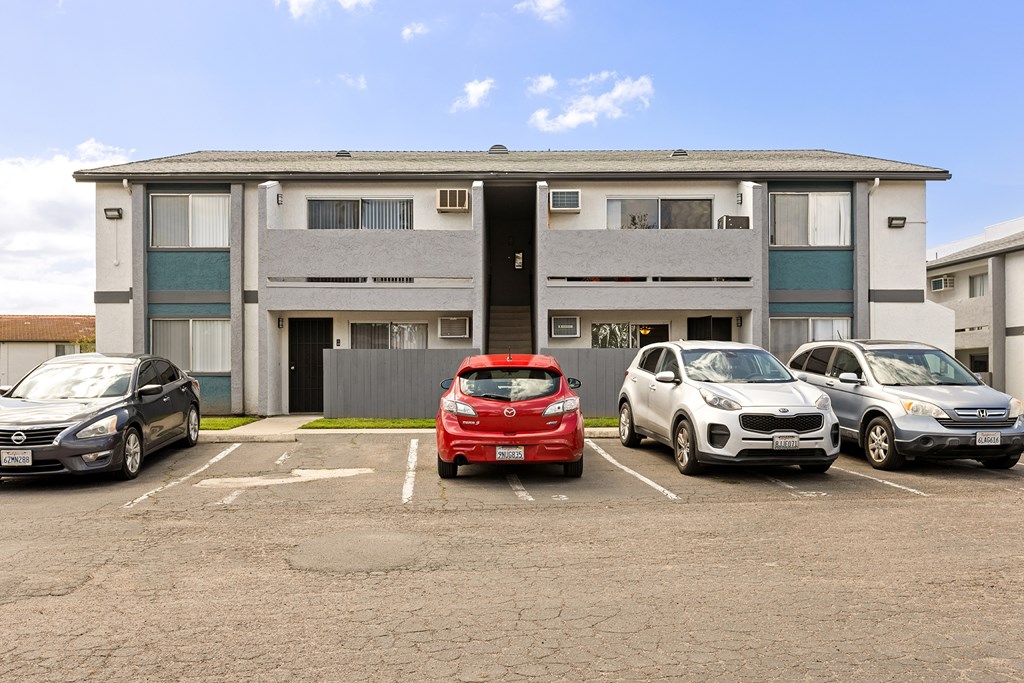 A parking lot with several cars parked in front of a multi-story apartment building.