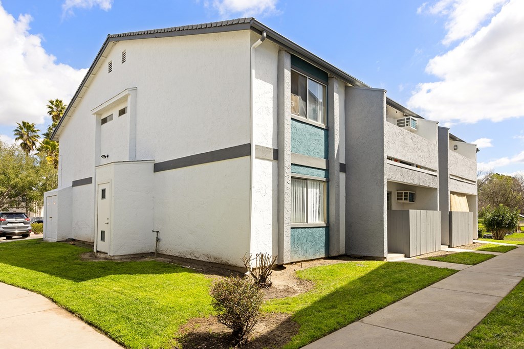 A white building with a grey roof and a green bush in front.