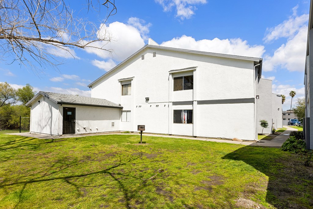 A white building with a black door and windows is surrounded by a green lawn.