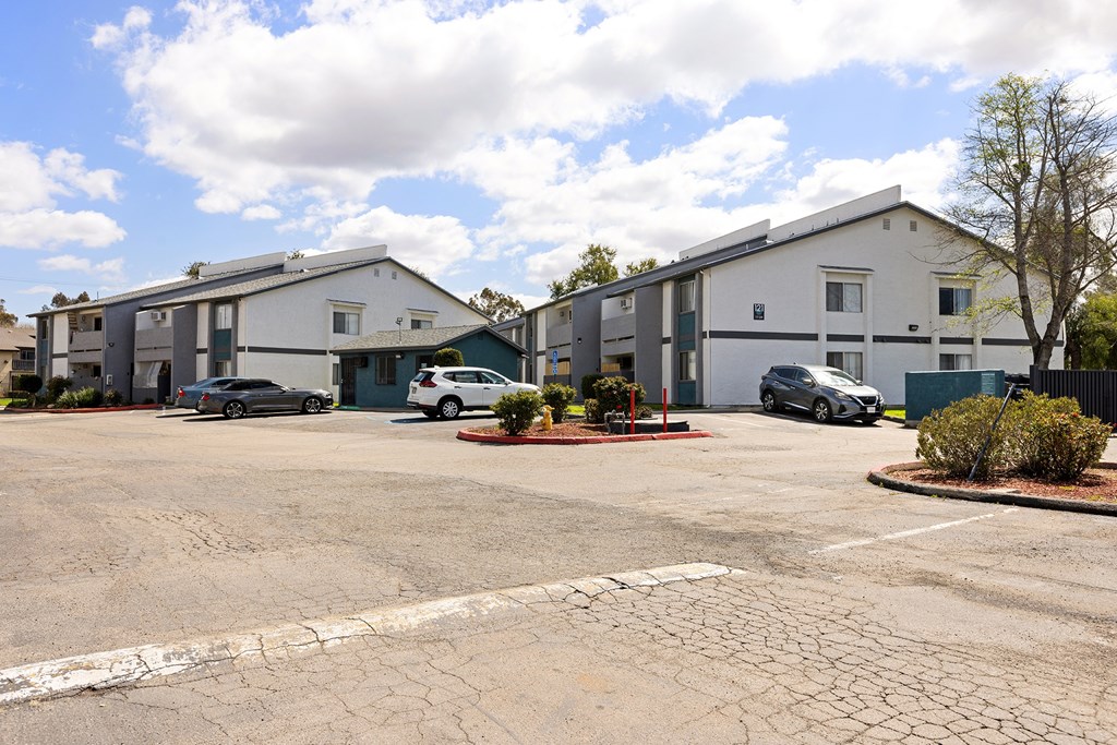 A parking lot in front of a building with a few cars parked.