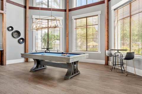 A pool table is in the middle of a room with a chair and a window.