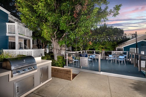 A patio with a grill and chairs is surrounded by trees.