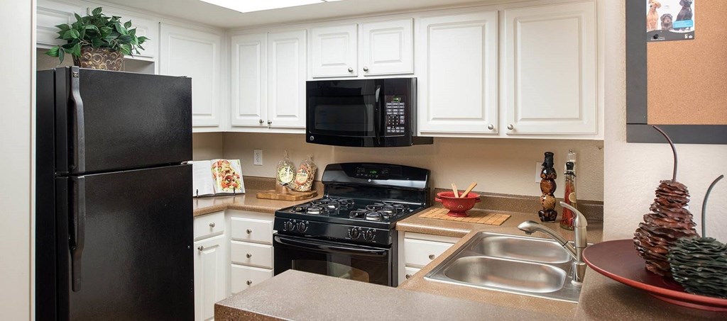 A black refrigerator sits in a kitchen with white cabinets.