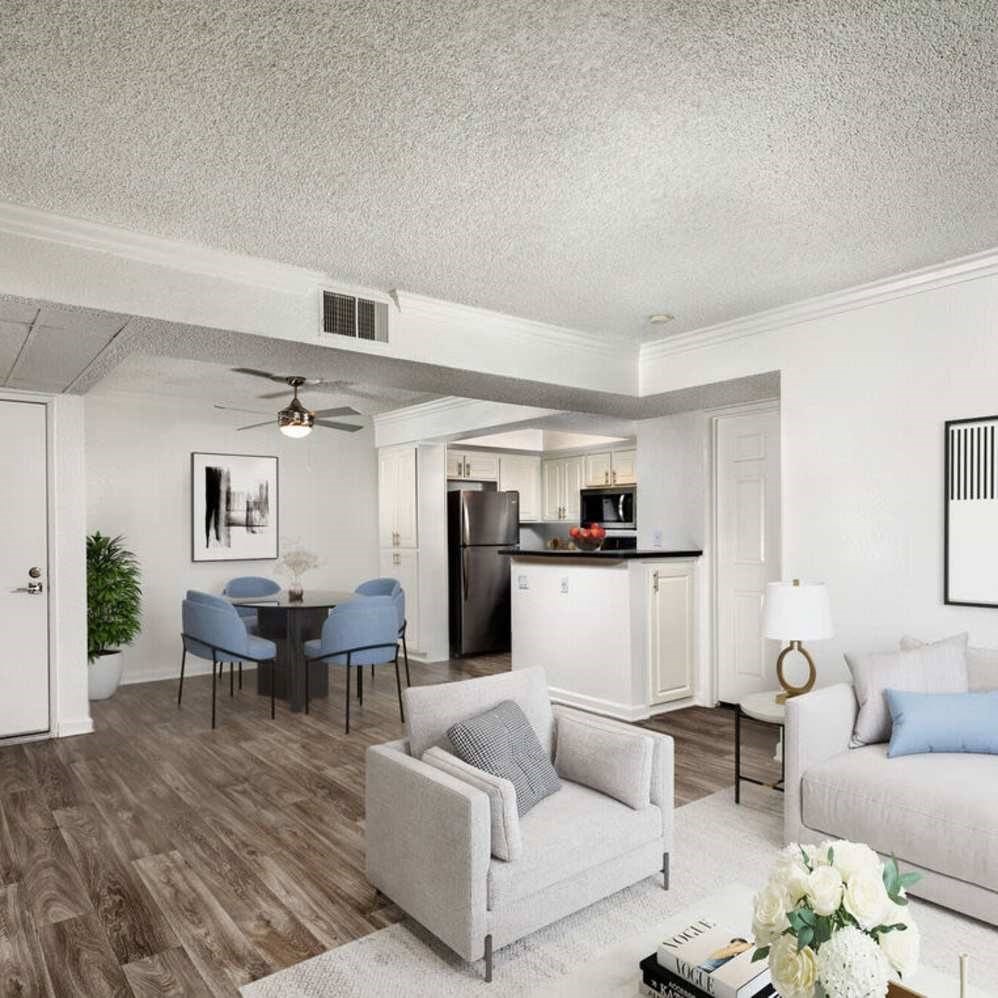 A living room with a grey couch, a dining table with chairs, a potted plant, and a vase of flowers on the coffee table.