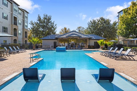 A swimming pool surrounded by lounge chairs and a pavilion in the background.