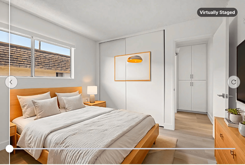 A bedroom with a large bed, a nightstand with a lamp, and a TV on the wall.