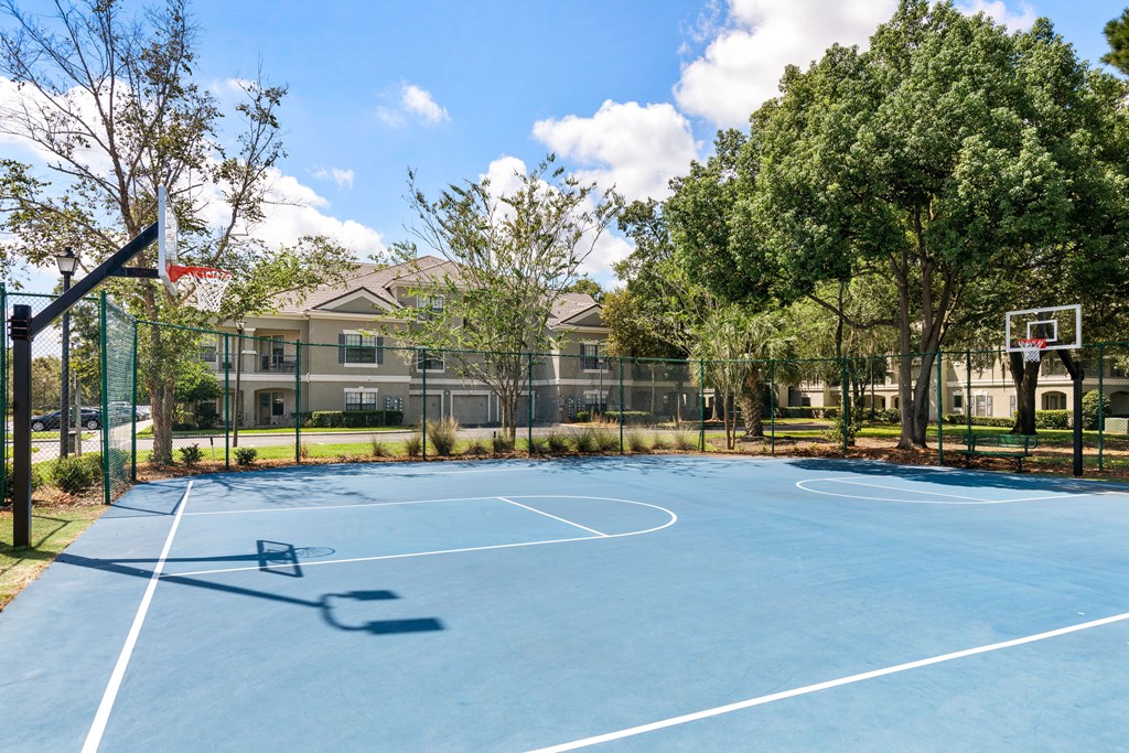 A basketball court is surrounded by a fence and trees.