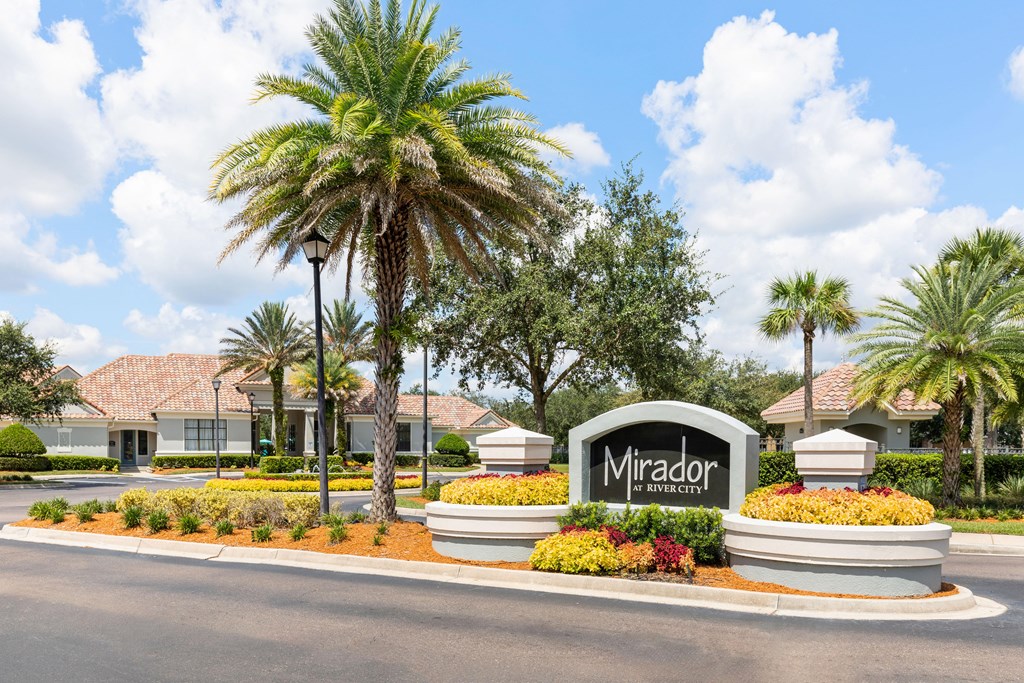 The entrance to the Mirador residential complex is surrounded by palm trees and landscaping.
