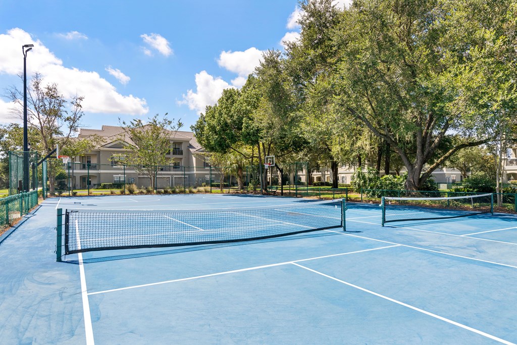 A tennis court surrounded by trees and a building in the background.