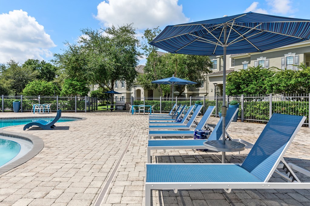 A pool area with sun loungers and a blue umbrella.